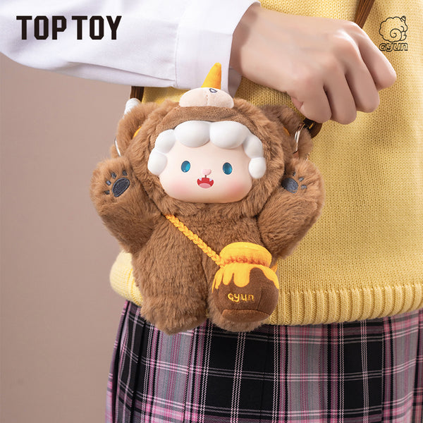 Plush toy keychain with a bear-like design held by a person wearing a yellow sweater and plaid skirt.