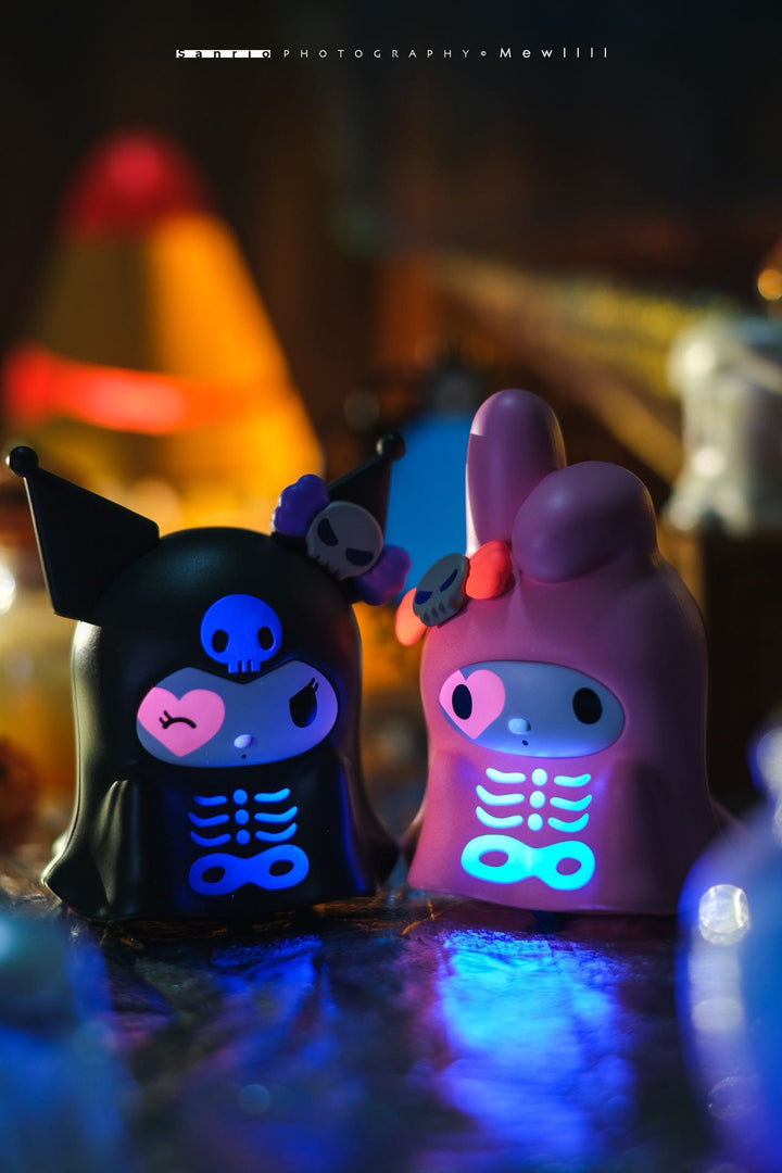 Two colorful skeleton-themed figurines with glowing eyes against a blurred neon background.